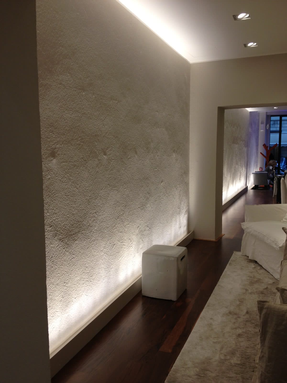 Showroom Gervasoni: parete materica illuminata di taglio e pavimento in rovere scuro.